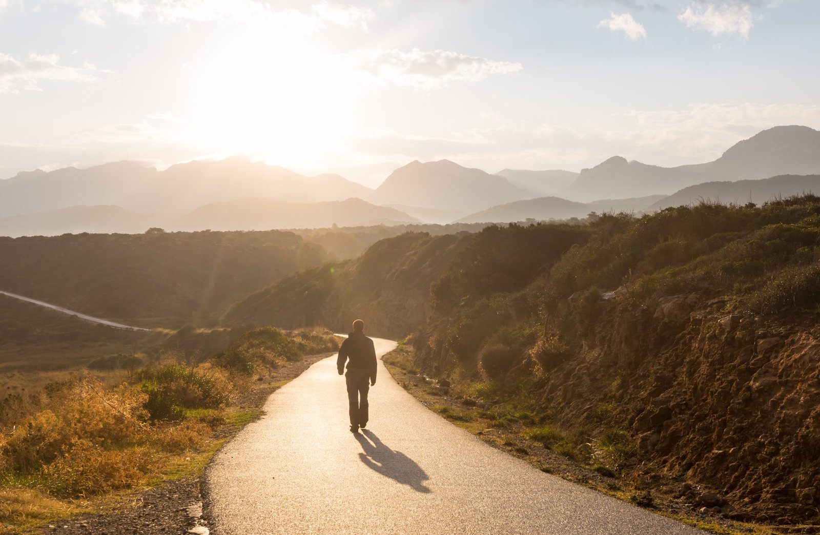 Scenic road in the mountains. Travel background. Man going on sunrise background.