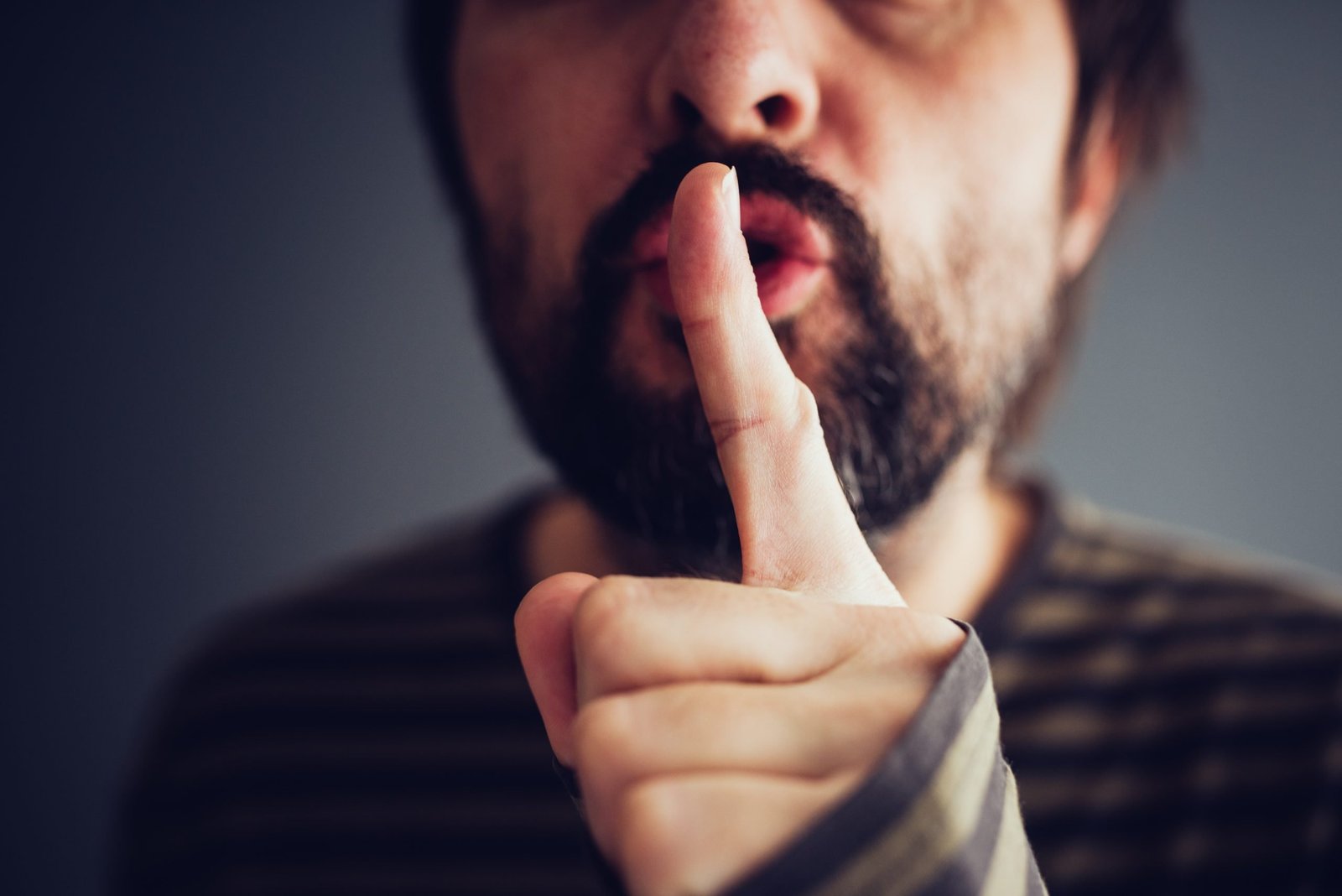 Man saying hush or be quiet with finger on lips, close up with selective focus