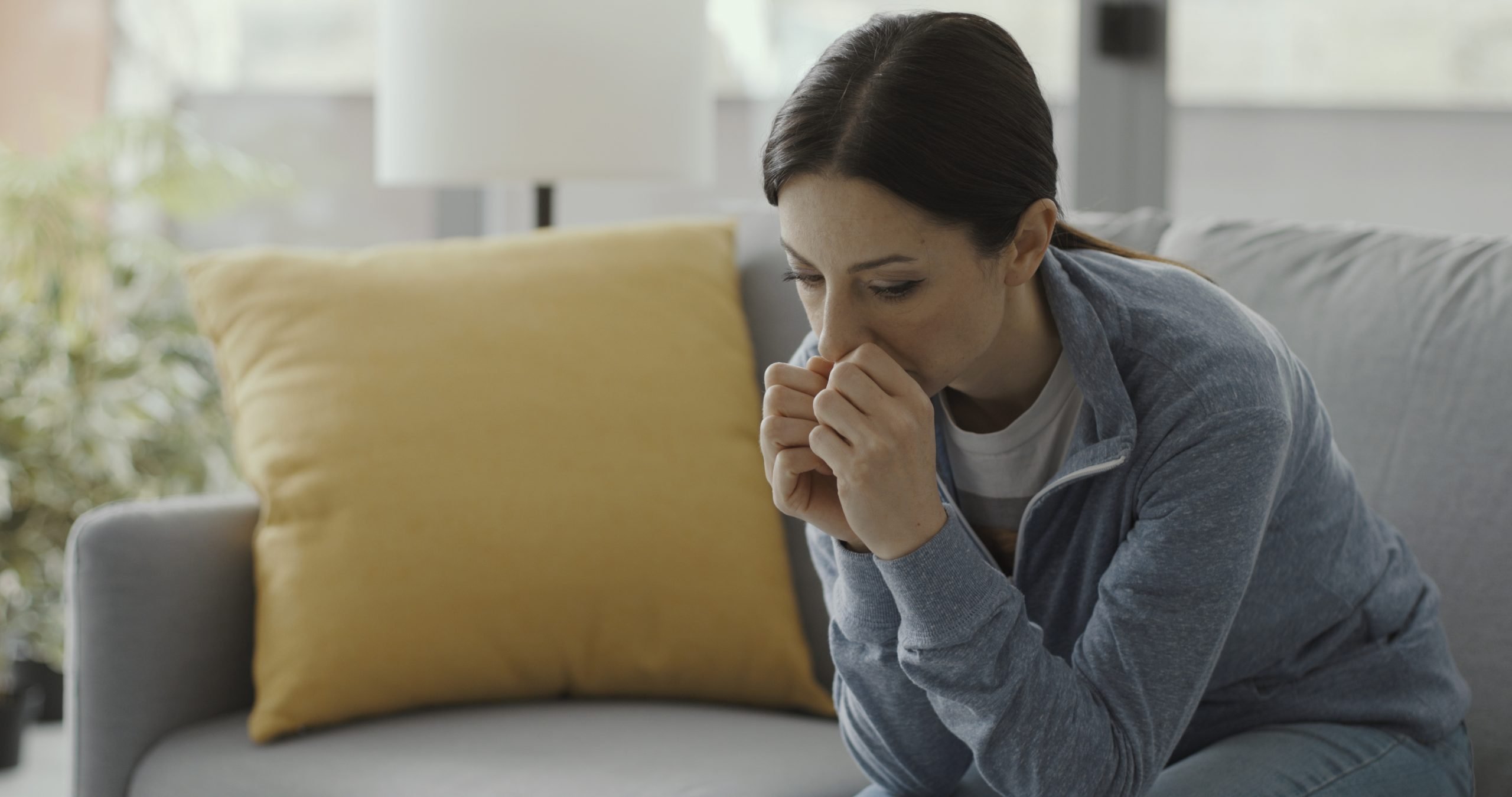 Sad depressed woman sitting on the couch self-isolating at home