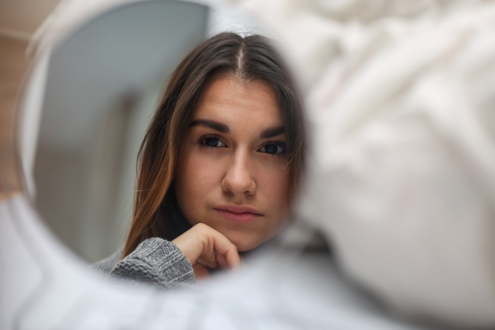 young beautiful girl looking in the mirror, a reflection of the different emotions,white bed in the background