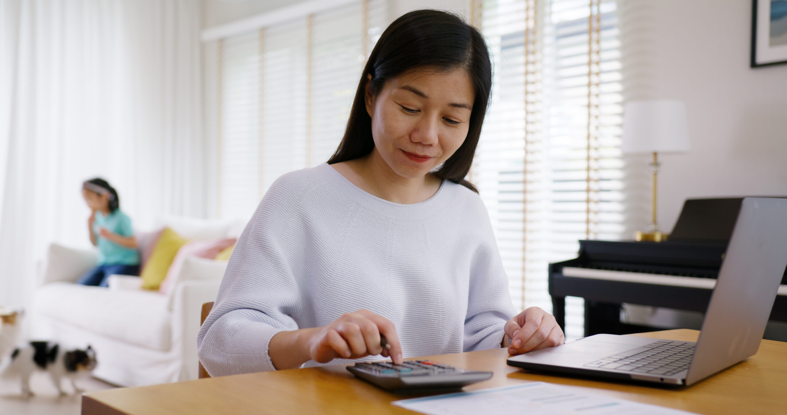 Adult asia people single mom small SME owner support happy sit busy apply child tax credit refund plan form app or pay loan bill on laptop. Little kid girl play at home hybrid job career workforce.